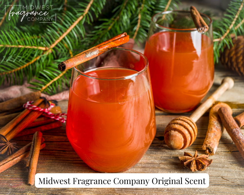 Two clear glasses of holiday wassail surrounded by cinnamon, spices, and pine branches on a rustic wood surface.