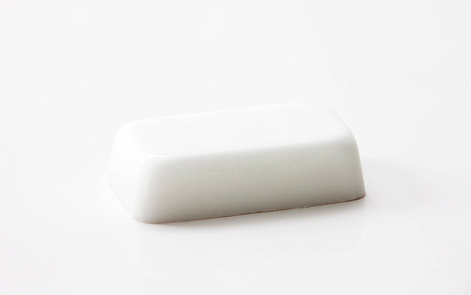 A smooth white bar of soap in partial shadow on a stark white background, depicting a goat's milk soap base.