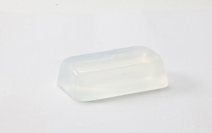 A clear bar of soap in partial shadow on a stark white background depicting a soap base sold by Midwest Fragrance Company.