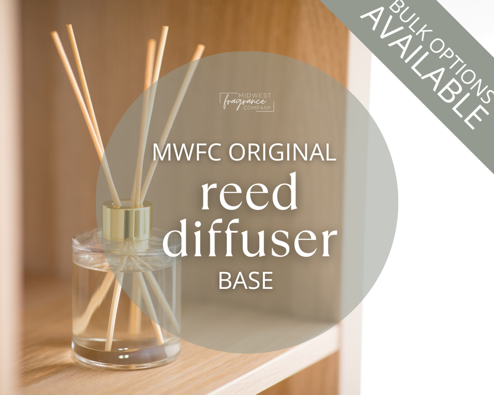A clear glass reed diffuser bottle with reeds on a white coffee table in a living room with a modern aesthetic. A reed diffuser base DIY friendly