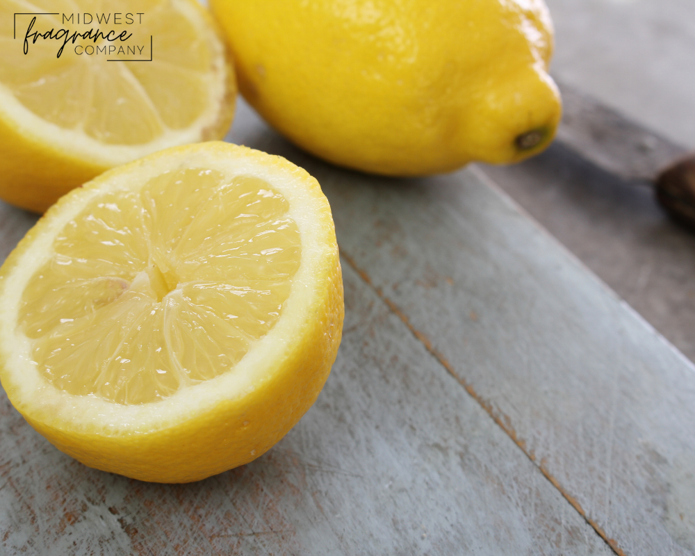 Fresh lemons, cut and whole, on a wooden cutting board with a knife in the background, indicating a fresh clean fragrance.