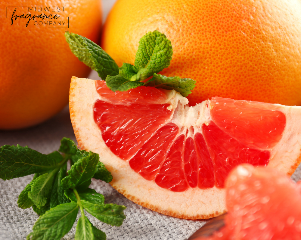 Sliced, fragrant pink grapefruit and mint leaves on a light woven mat with whole grapefruits in the background.