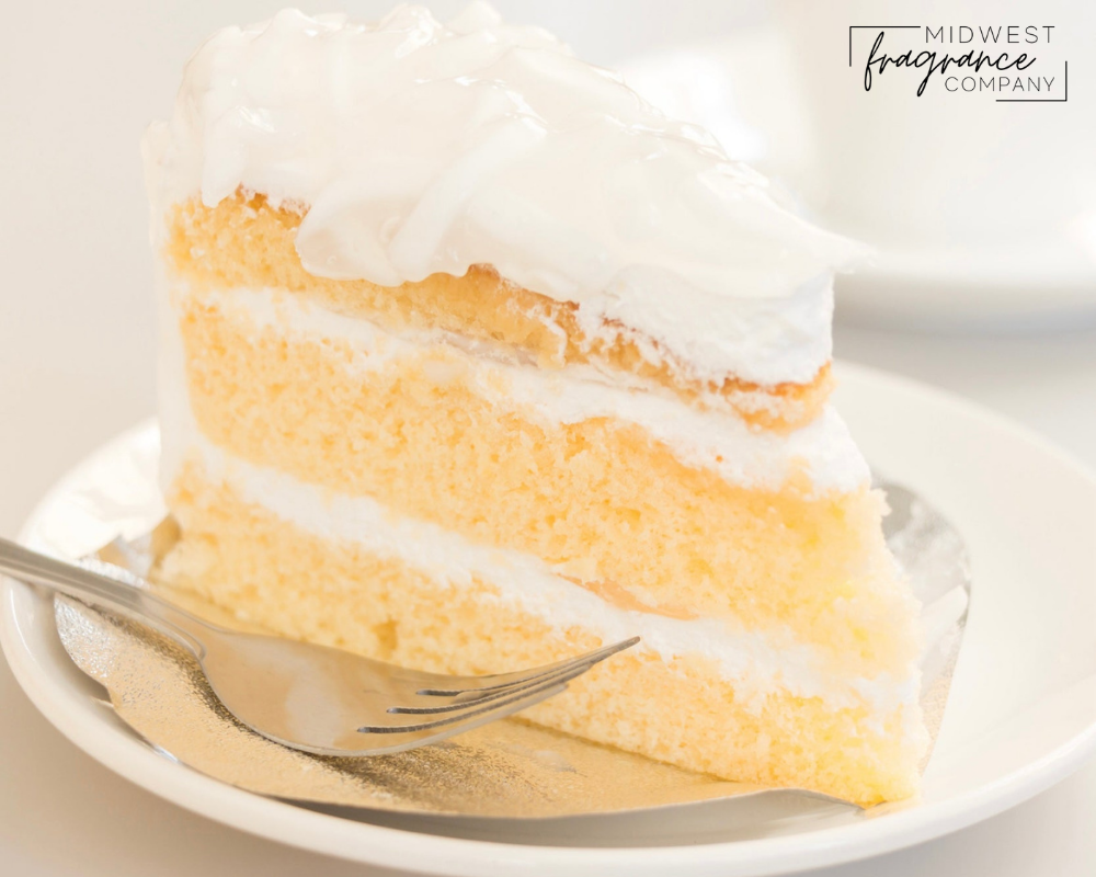A piece of three layer white cake with icing on a white ceramic plate and silver fork on a white blurred background.