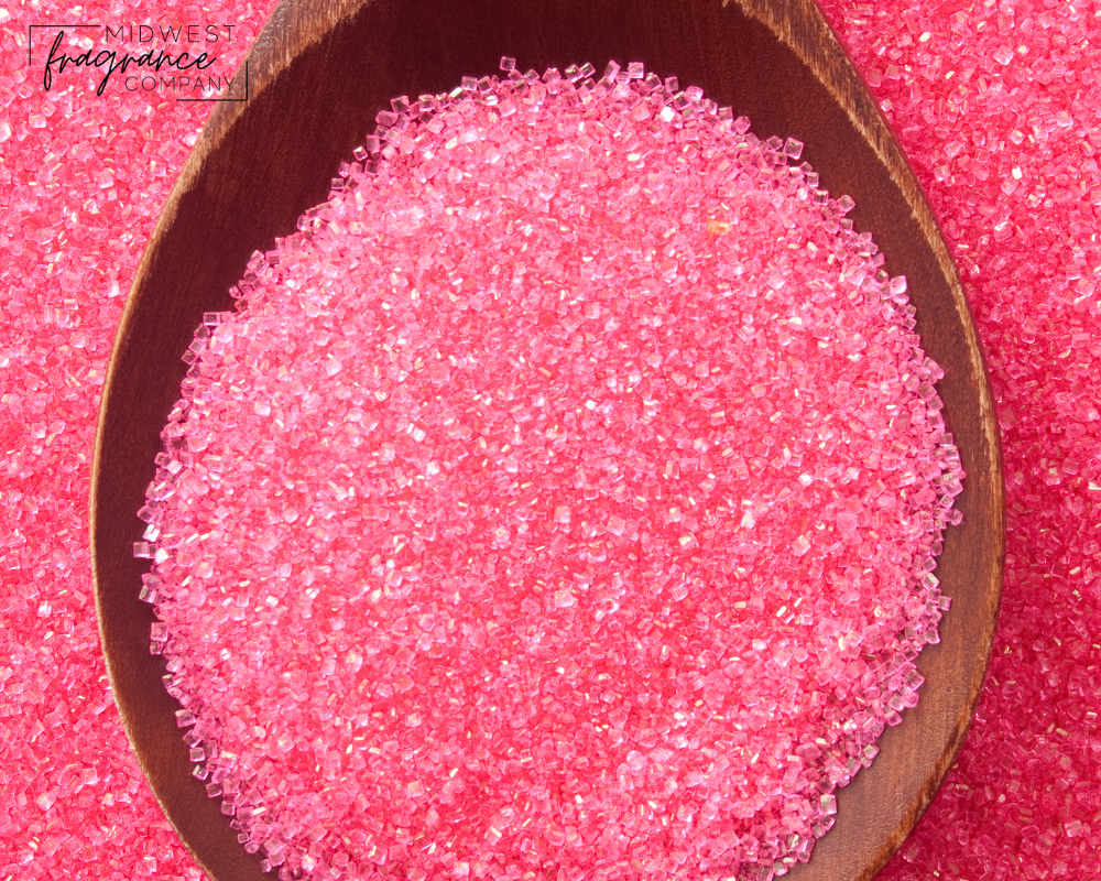 A wooden spoon full of pink colored sugar crystals, evoking the scent of sweet berries and delicate florals.