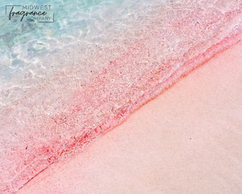 Light, fine pink sand flowing into a light turquoise sea on a beach evoking feelings of tropical fruits and greens.