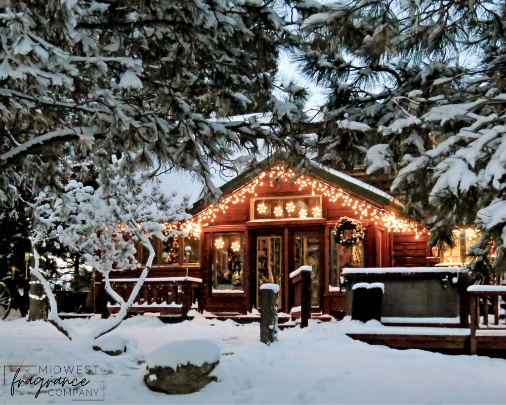A Christmas Cabin with white twinkling lights and wreath set in a snowy landscape.