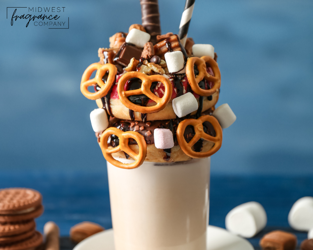 An elaborate salted pretzel milkshake with cookies, marshmallows, chocolate and a straw on a blue background.