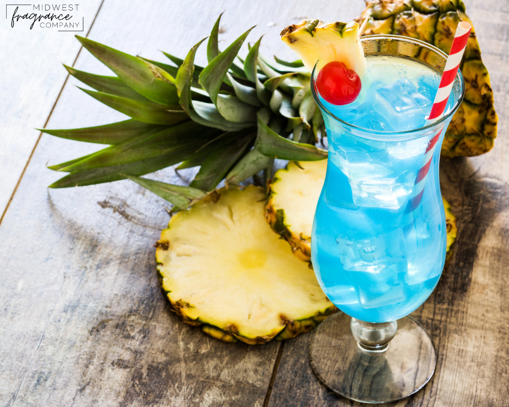 Large clear hurricane glass of blue hawaiian punch with ice, a cherry, straw, and pineapple slices on a rustic wooden surface.