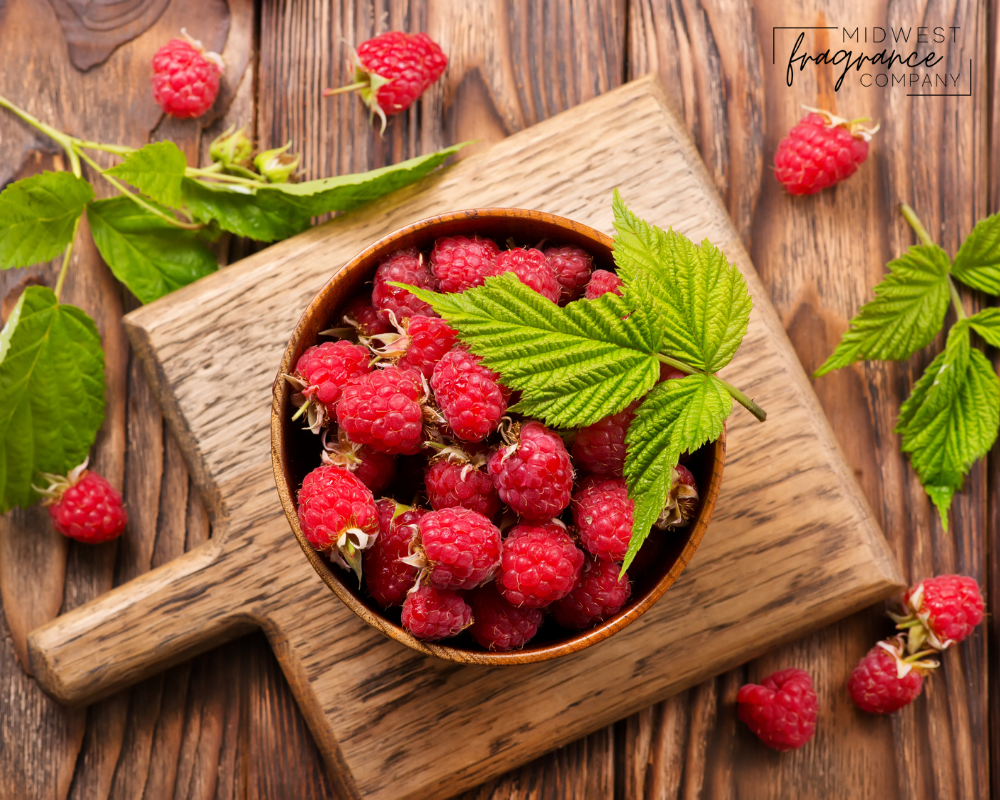 A wooden bowl of fresh red raspberries with wild honeysuckle leaves on a rustic wood table.